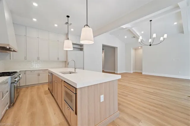 a kitchen with a sink a chandelier stainless steel appliances cabinets and a counter top space