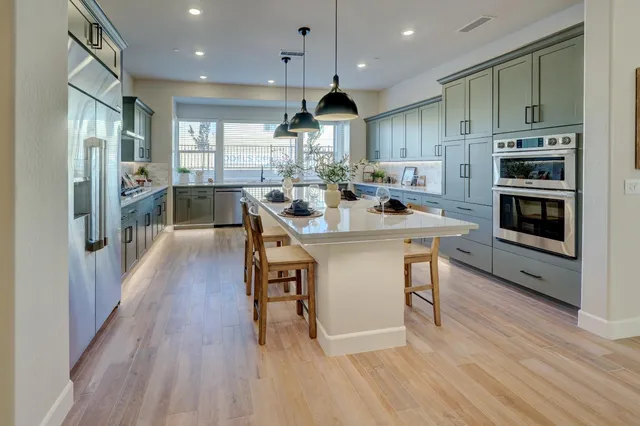 a kitchen with stainless steel appliances a dining table chairs stove refrigerator and cabinets