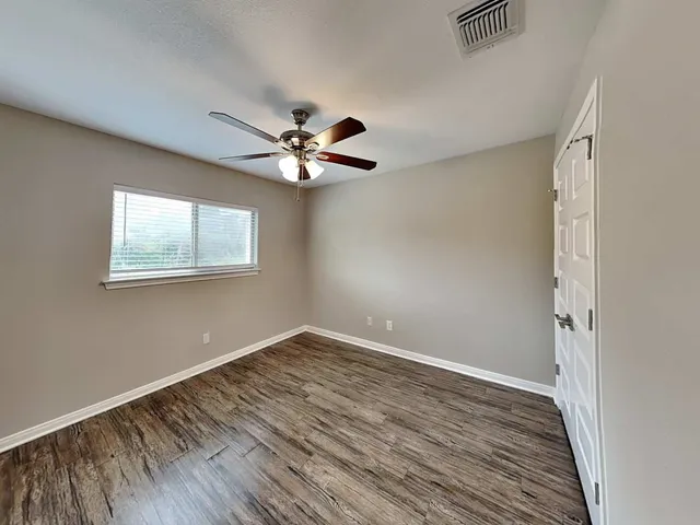 an empty room with wooden floor chandelier fan and windows