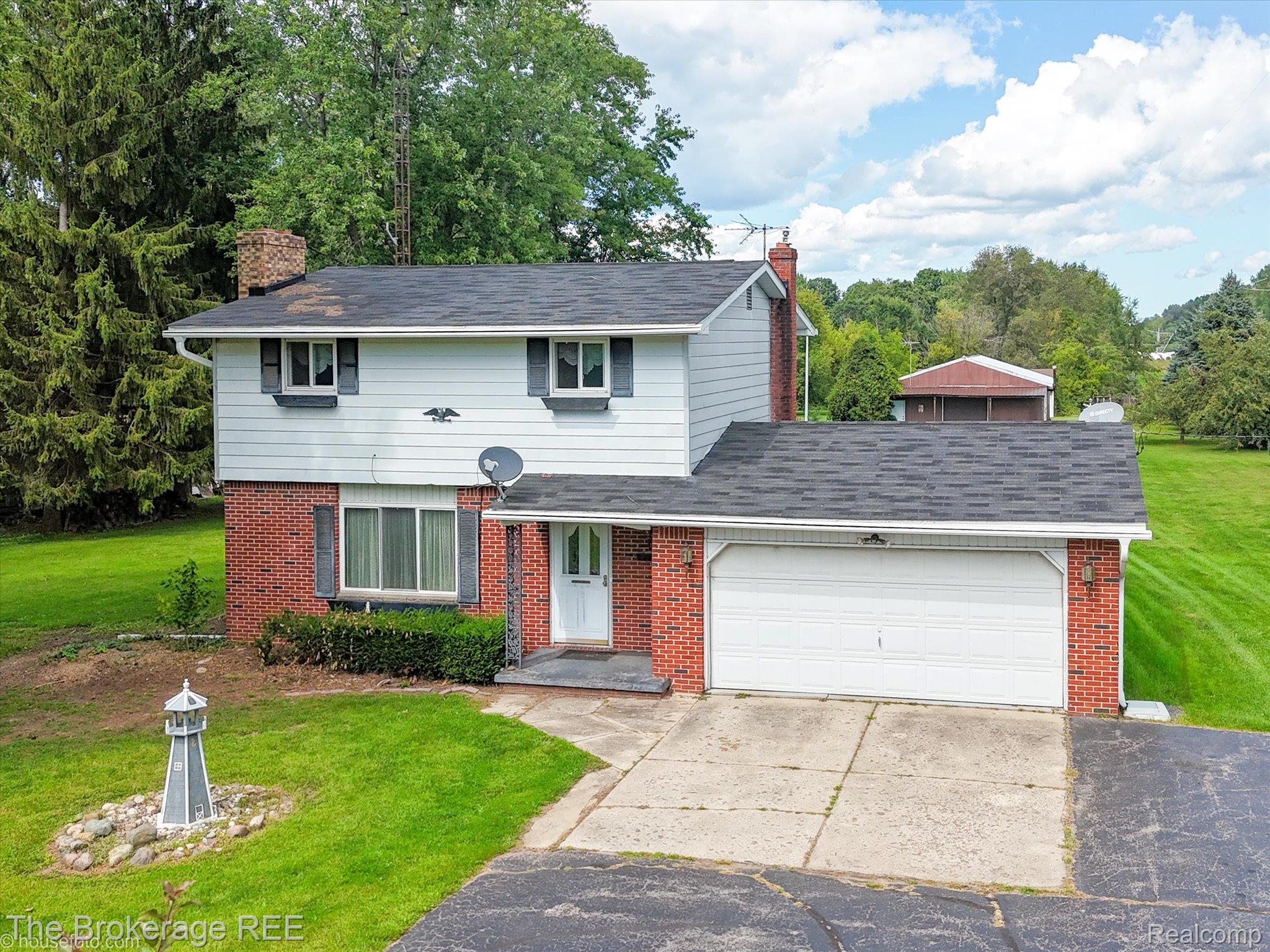 6129 East Lake Road Millington, MI 48746 - Photo 2 of 47 View of front of home with a front yard, an attached garage, brick siding, driveway, and a chimney