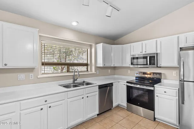 a kitchen with white cabinets appliances a sink and a window