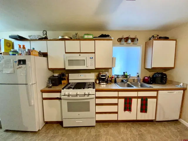 a white kitchen with stainless steel appliances a stove a refrigerator a sink a counter space and cabinets