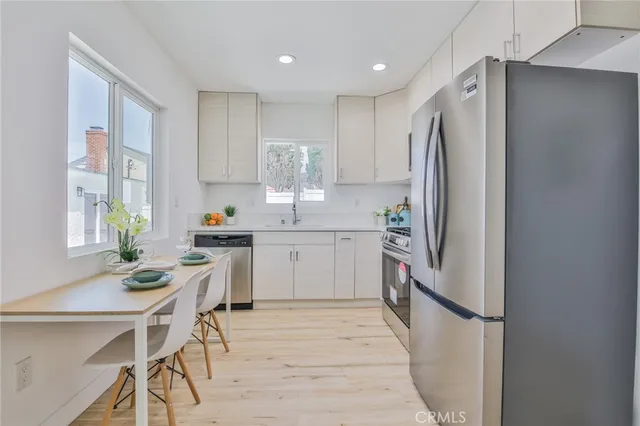 a kitchen with a refrigerator a stove a sink dishwasher and a dining table with wooden floor