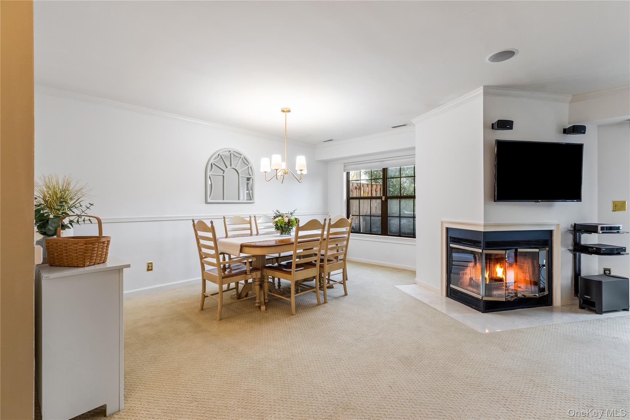 17 Sutton Place Islip, NY 11751 - Photo 13 of 32 Dining space with crown molding, light colored carpet, a multi sided fireplace, and a chandelier