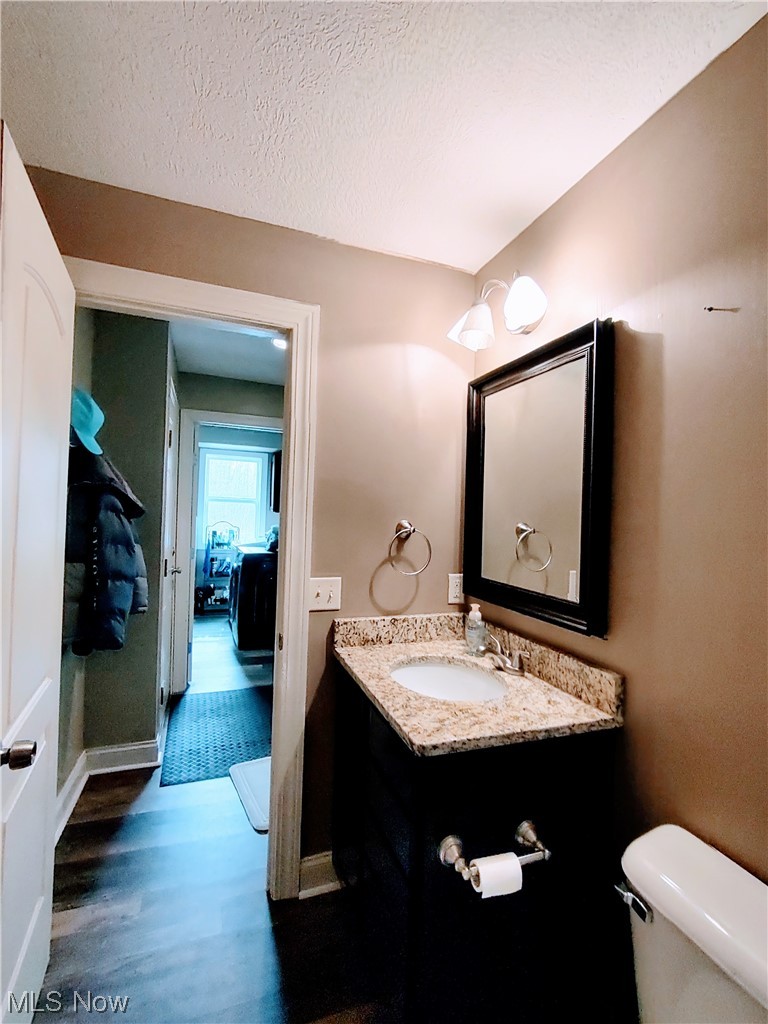 1468 Steese Road Uniontown, OH 44685 - Photo 14 of 28 Bathroom featuring wood-type flooring, vanity with extensive cabinet space, a textured ceiling, and toilet