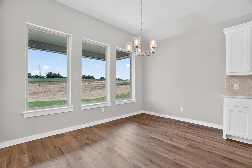 504 Clifton Court Springtown, TX 76082 - Photo 15 of 36 Interior space featuring three rectangular windows, wood-finish flooring, a contemporary chandelier, white baseboards, and built-in white cabinetry with a patterned backsplash