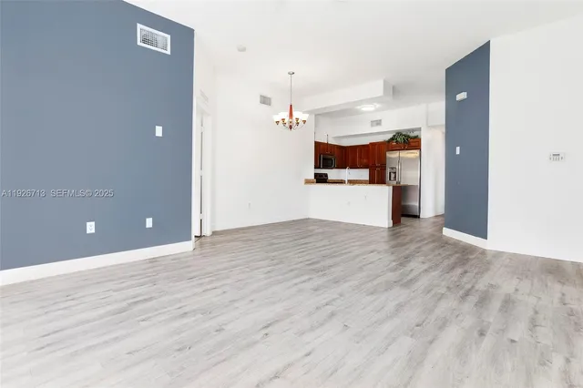 an empty room with wooden floor and kitchen view