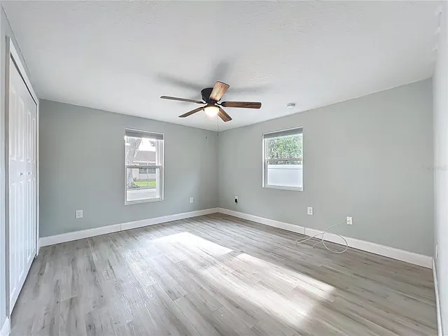 an empty room with wooden floor chandelier fan and windows