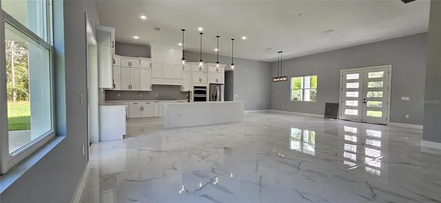 a large white kitchen with granite countertop a stove a sink a refrigerator and white cabinets with wooden floor