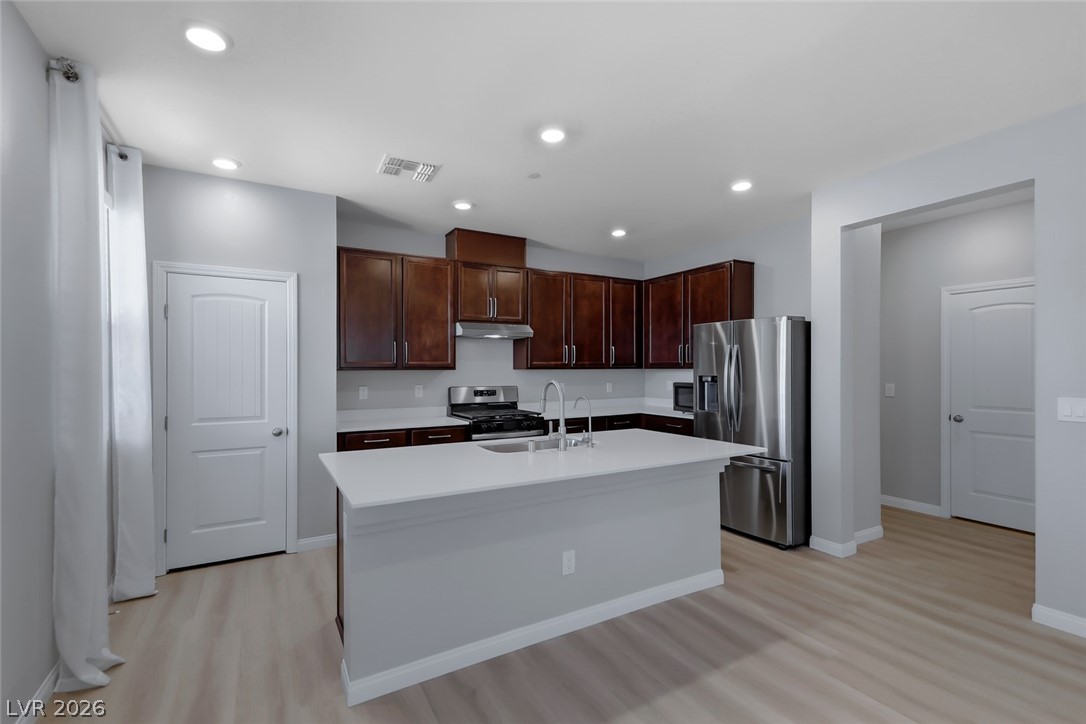 3564 Credere Lane Henderson, NV 89074 - Photo 9 of 40 Kitchen with stainless steel appliances, dark wood finish cabinets, light wood-type flooring, an island with sink, and recessed lighting