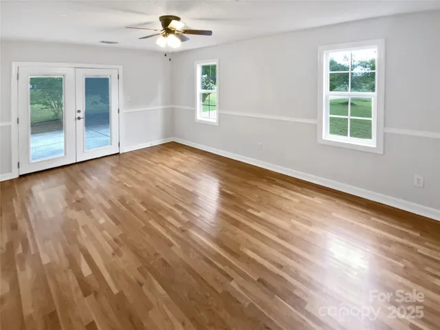 an empty room with wooden floor chandelier fan and windows