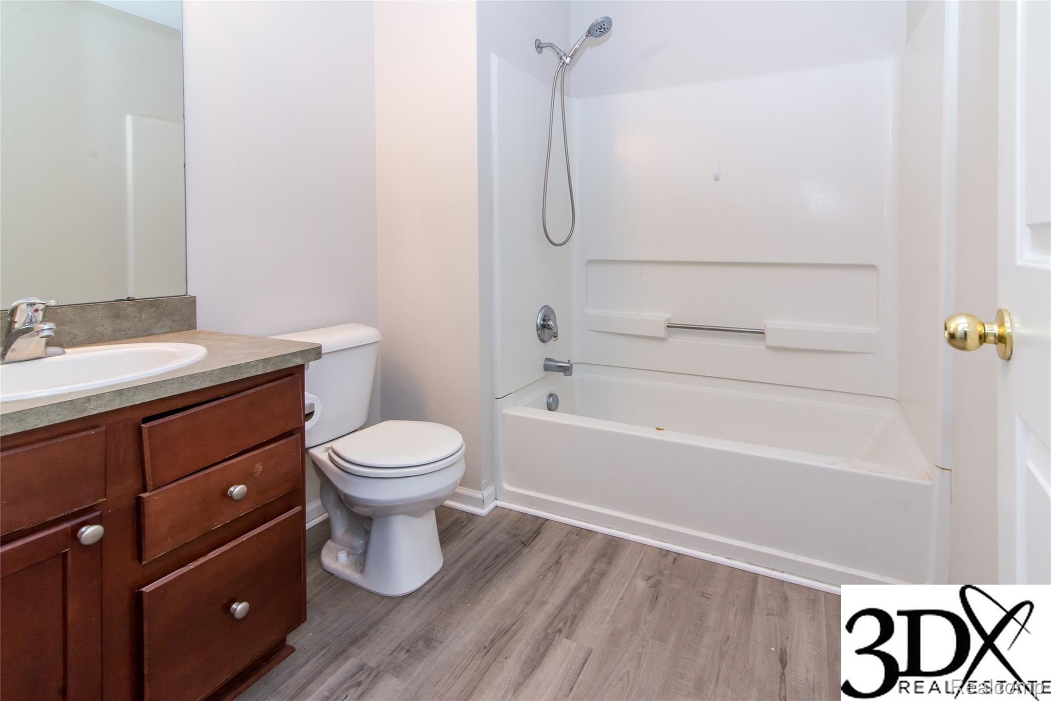 4256 Hampton Ridge Boulevard Howell, MI 48843 - Photo 18 of 25 Wood-finish flooring, white bathtub with shower, dark wood-finish vanity with countertop, and an oval sink with a chrome faucet