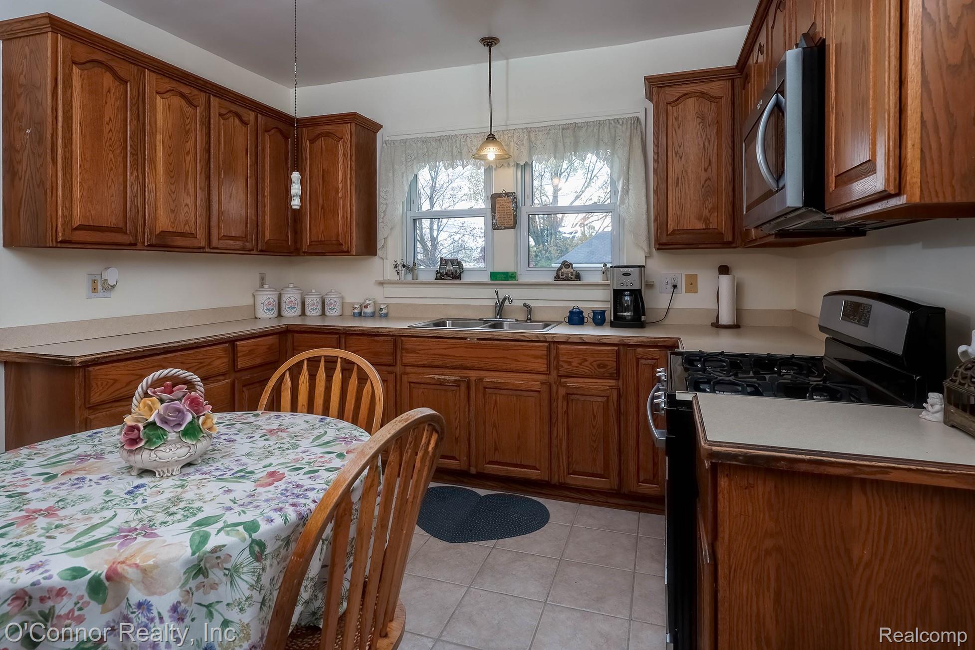 3323 Kinney Road Emmett, MI 48022 - Photo 12 of 29 Kitchen featuring extensive wood cabinetry, L-shaped laminate countertops, a stainless steel microwave, a black gas range, and a window above the sink