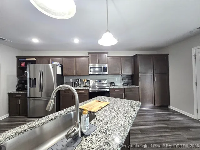 a kitchen with stainless steel appliances granite countertop a refrigerator a stove and a sink with wooden floor