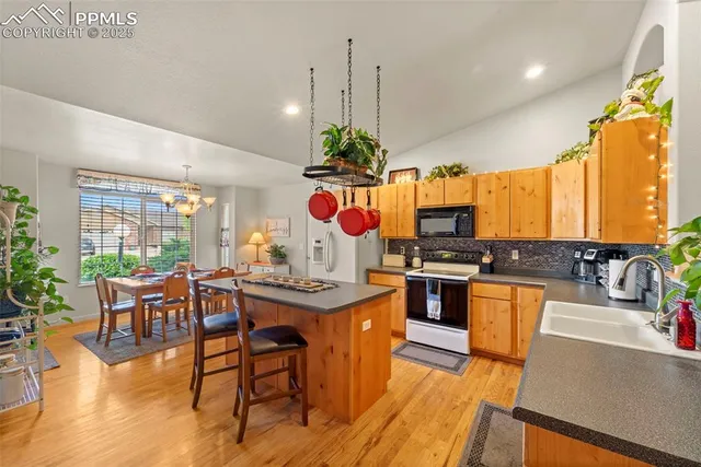 a kitchen with stainless steel appliances granite countertop a stove top oven a sink dishwasher a dining table and chairs with wooden floor