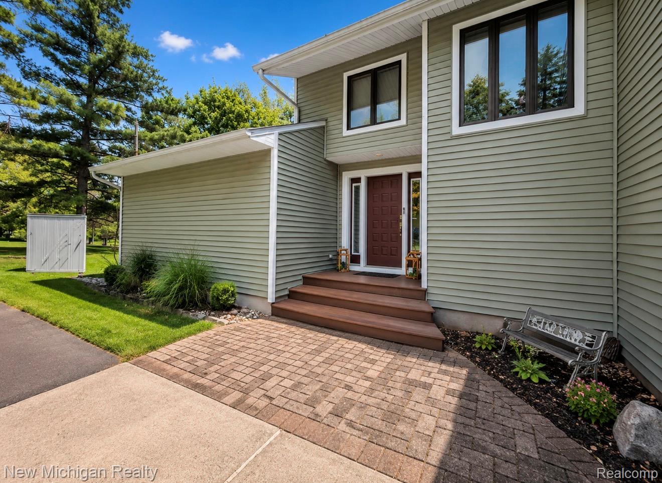 7156 East River Road Flushing, MI 48433 - Photo 2 of 35 Contemporary exterior featuring light green siding, a paneled front door with sidelights, and dark-framed windows