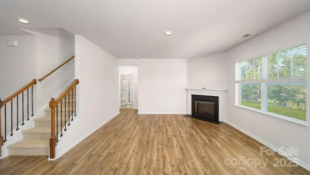 a view of an empty room with wooden floor fireplace and a window