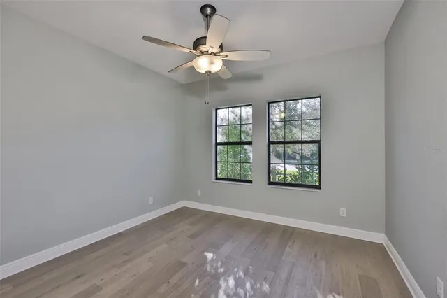 an empty room with wooden floor chandelier fan and windows