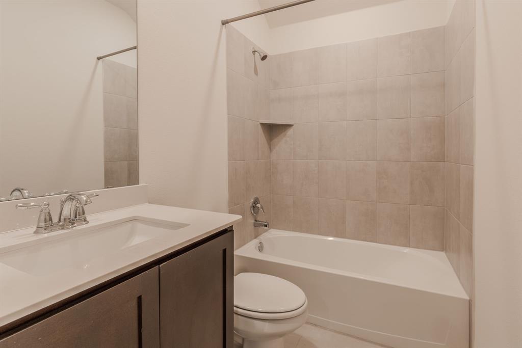 2902 Trusting Way Aubrey, TX 76227 - Photo 18 of 38 Bathroom featuring a white bathtub with tile surround, a built-in shower niche, a chrome showerhead, a single vanity with a white countertop and integrated sink, and a chrome faucet