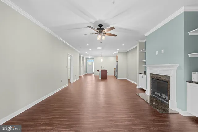 a view of an empty room and kitchen with fireplace ceiling fan