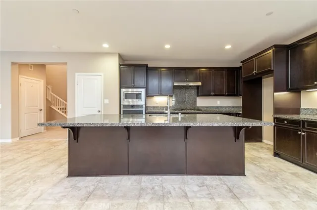 a large kitchen with stainless steel appliances kitchen island granite countertop a large counter top and a stove top oven
