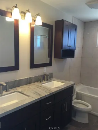 a bathroom with a double vanity sink and mirror with toilet