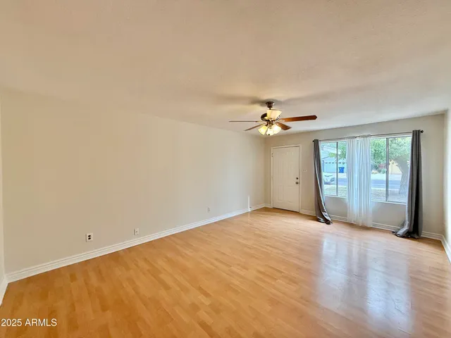 a view of empty room with wooden floor and fan