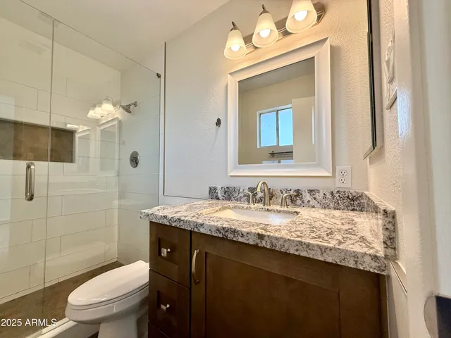 a bathroom with a granite countertop sink toilet a mirror and shower