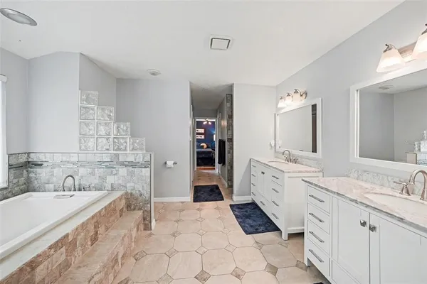 a large white bathroom with a granite countertop double vanity sink a mirror and a bathtub
