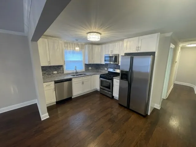 a kitchen with stainless steel appliances granite countertop a refrigerator a sink dishwasher a stove top oven a wooden floor and cabinets