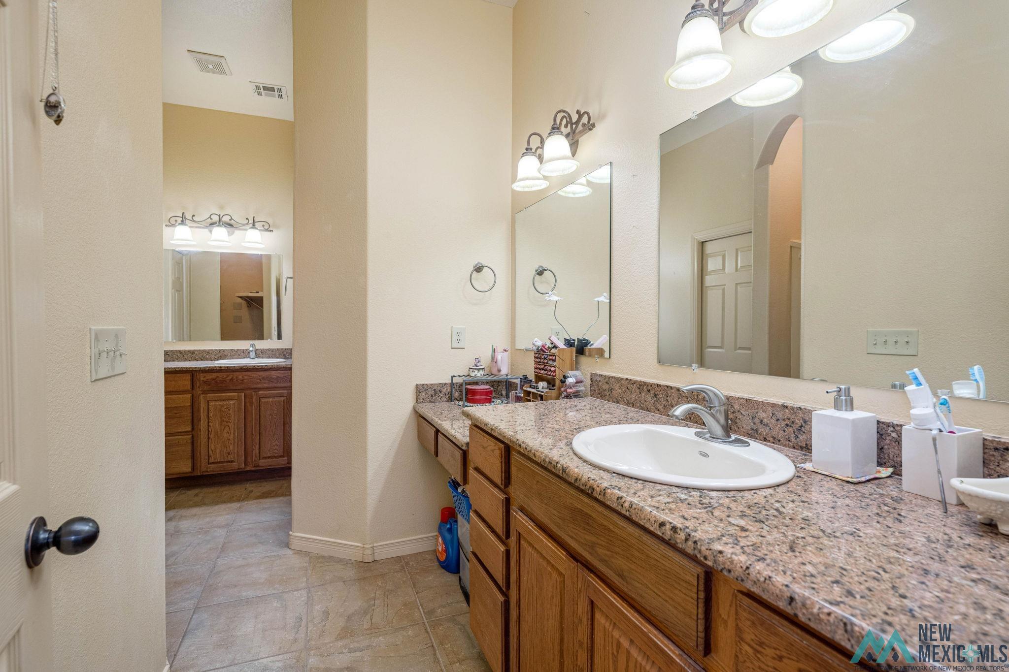 3884 Adriatic Road Las Cruces, NM 88012 - Photo 26 of 45 Double vanity bathroom featuring granite countertops, wood-finish cabinetry, ceramic tile flooring, and integrated lighting fixtures