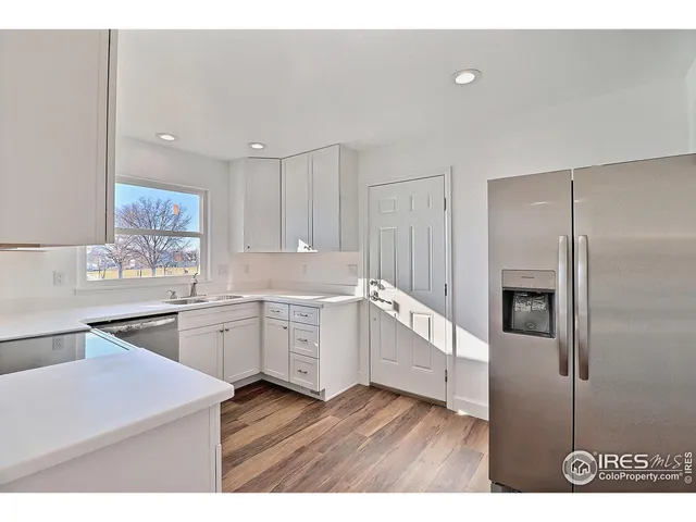 a kitchen with granite countertop a refrigerator a sink dishwasher and white cabinets with wooden floor