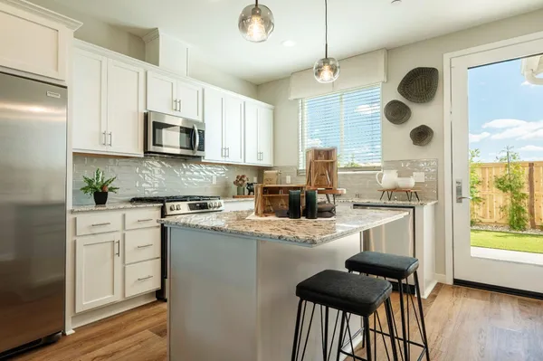 a kitchen with stainless steel appliances granite countertop a stove a sink a microwave oven a refrigerator with white cabinets and wooden floor