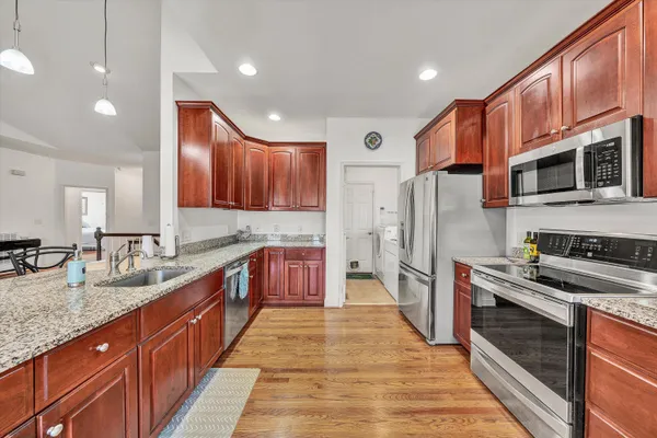a kitchen with stainless steel appliances granite countertop wooden cabinets a sink a stove a dining table and chairs