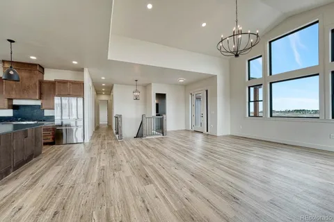 a view of an empty room and kitchen with wooden floor