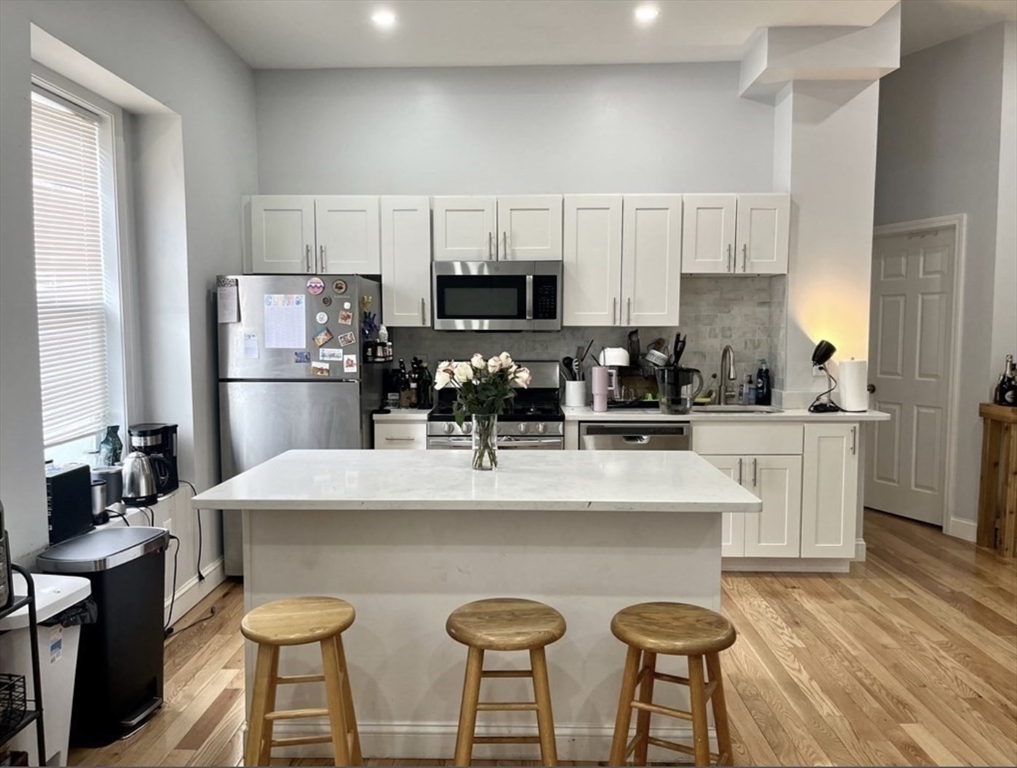 83 Highland Street, Unit 1 Boston, MA 02119 - Photo 2 of 9 a kitchen with stainless steel appliances a white table chairs refrigerator and microwave