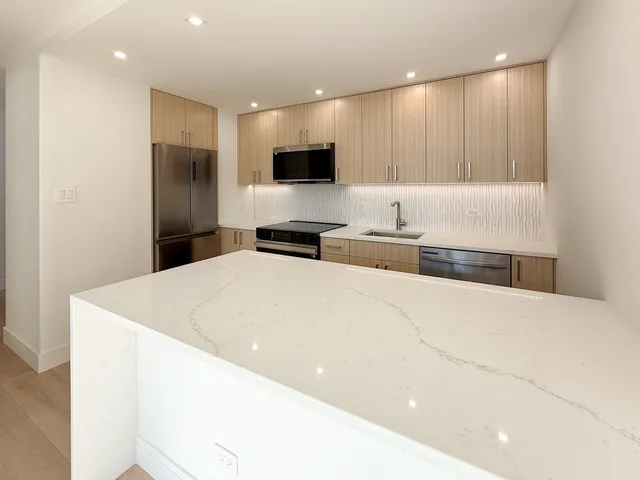 a large white kitchen with kitchen island a sink stainless steel appliances and cabinets