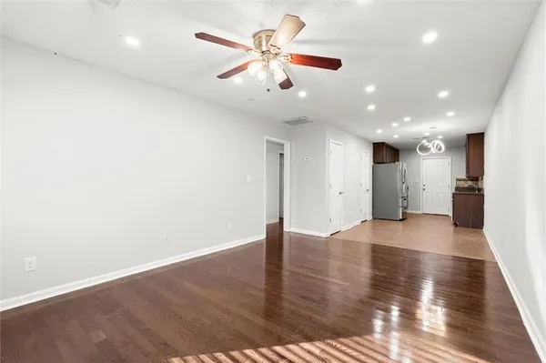 a view of an empty room with wooden floor and a ceiling fan