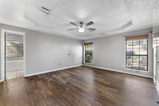 an empty room with wooden floor chandelier fan and windows
