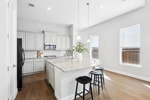 a kitchen with kitchen island granite countertop a stove a sink a refrigerator and white cabinets with wooden floor
