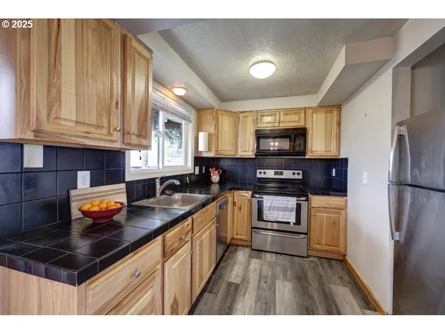 a kitchen with granite countertop stainless steel appliances a stove a sink a refrigerator cabinets and a window
