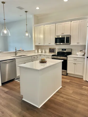 a kitchen with stainless steel appliances granite countertop a sink a stove a refrigerator and white cabinets with wooden floor