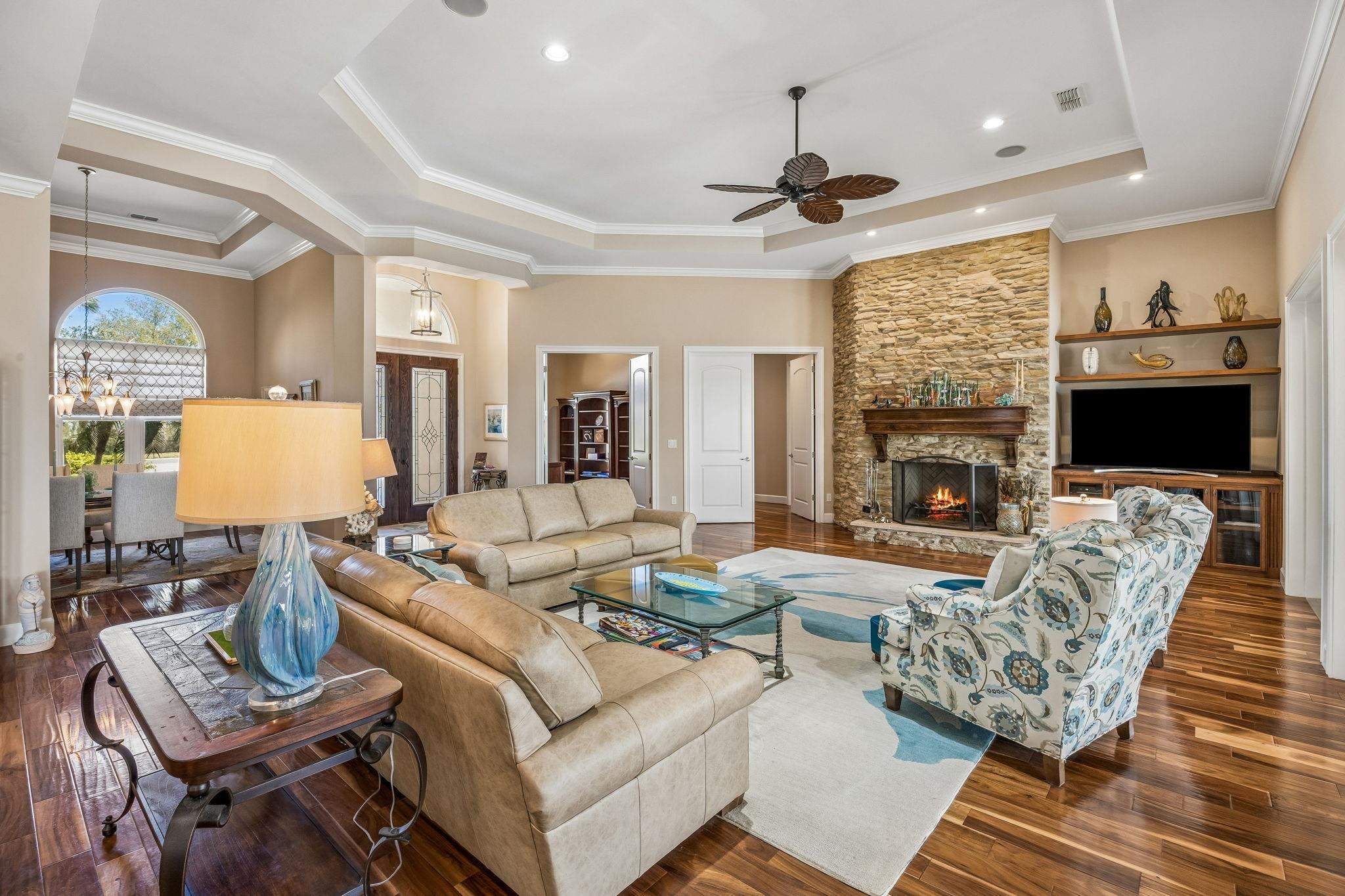 409 Lookout Point Drive St. Augustine, FL 32080 - Photo 16 of 90 Living room featuring dark wood-style floors, a tray ceiling, a ceiling fan, a stone fireplace, and ornamental molding
