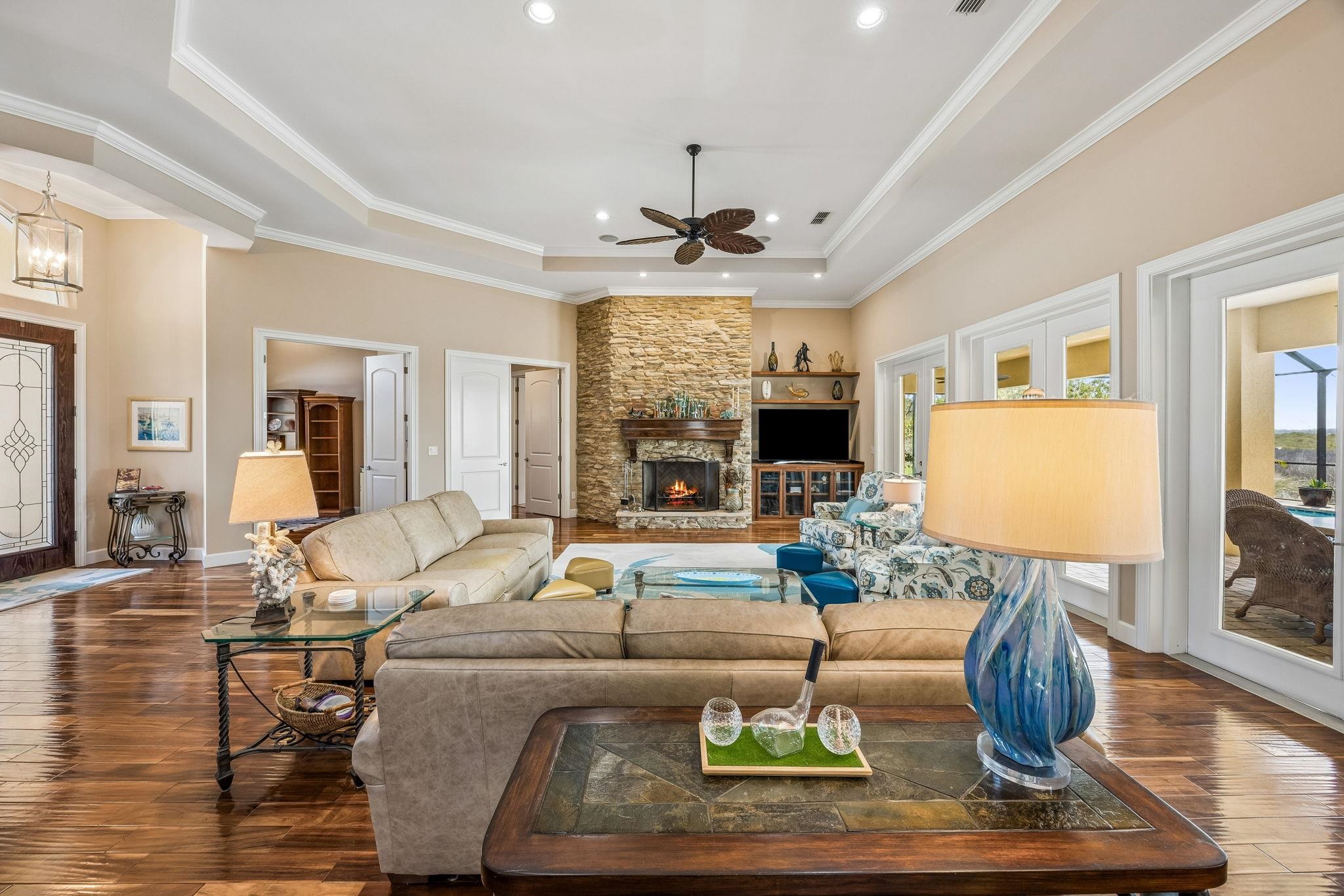 409 Lookout Point Drive St. Augustine, FL 32080 - Photo 17 of 90 Living room with wood-type flooring, a ceiling fan, a stone fireplace, a tray ceiling, and ornamental molding