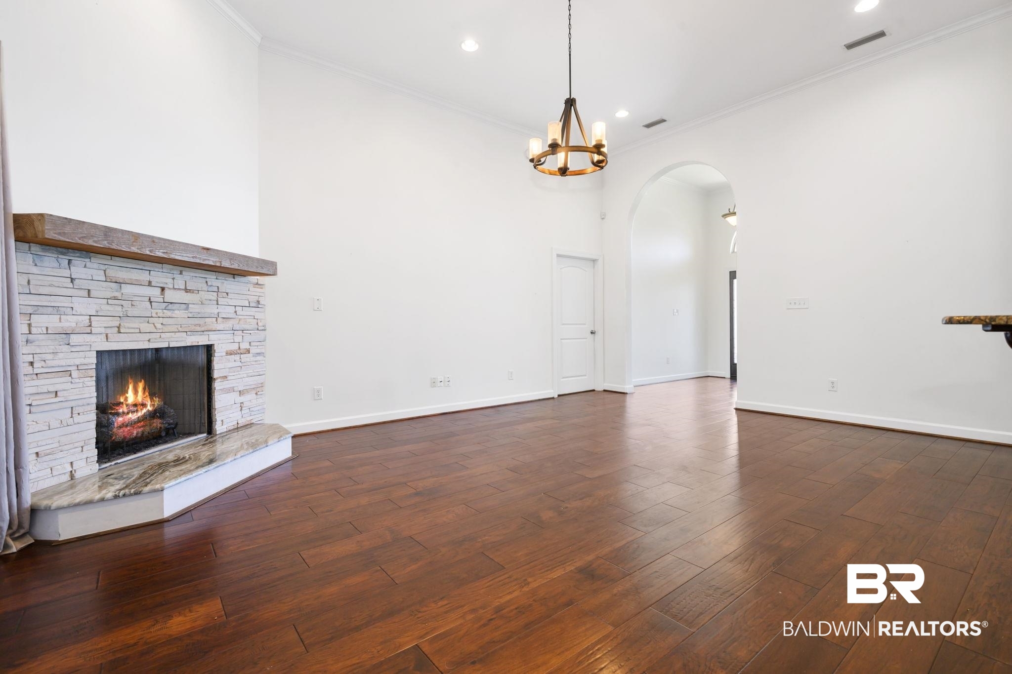 9730 Harmony Ridge Circle West Semmes, AL 36575 - Photo 5 of 38 Unfurnished living room with arched walkways, ornamental molding, dark wood-type flooring, a stone fireplace, and a chandelier