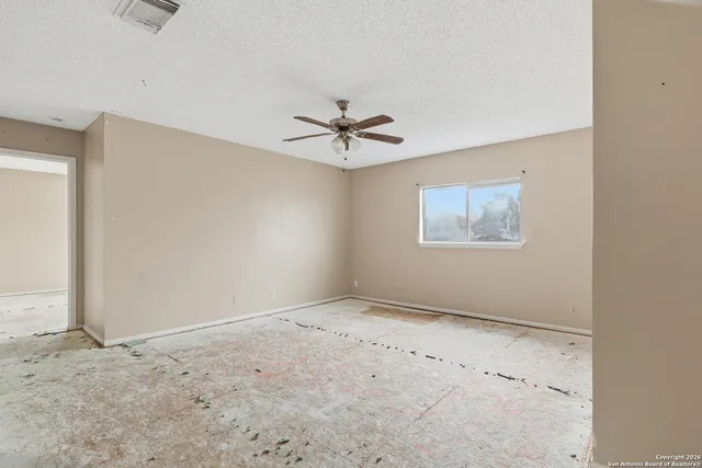 an empty room with chandelier fan and windows