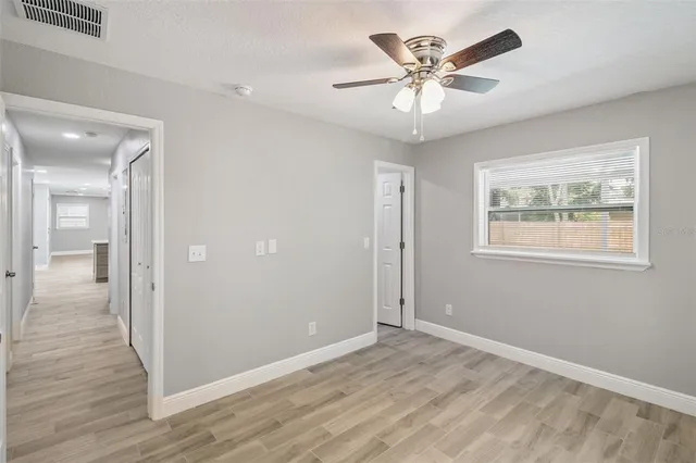 a view of an empty room with wooden floor and a ceiling fan
