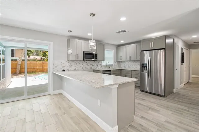 a large kitchen with stainless steel appliances granite countertop a refrigerator a sink a stove a microwave and island with wooden floor