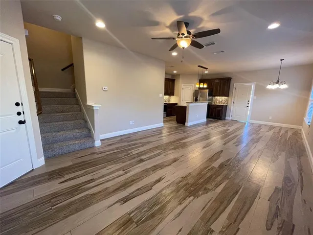 a view of an empty room with wooden floor and a ceiling fan