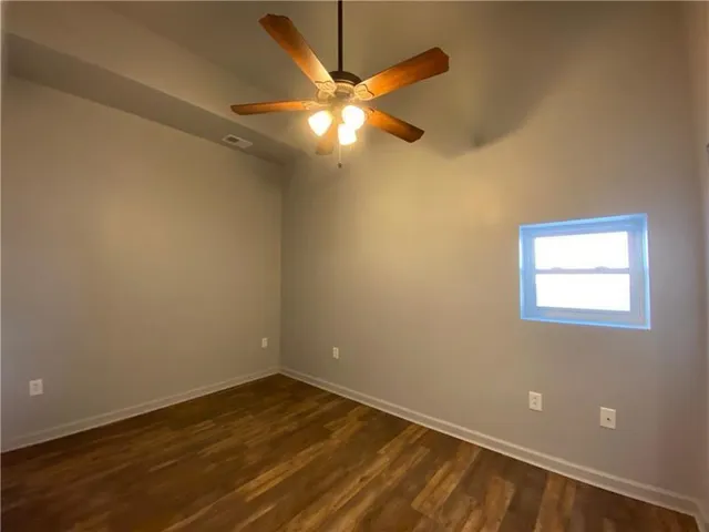 a view of an empty room with wooden floor and a ceiling fan